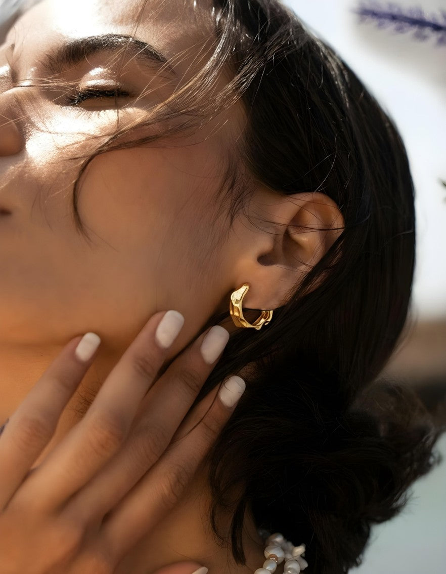 Model wearing sculptural gold Molten Muse hoop earrings